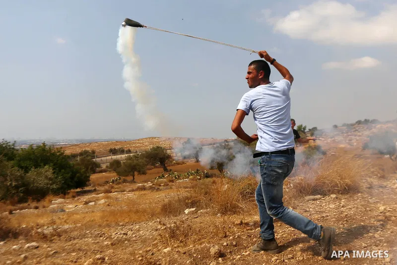 A Palestinian protester uses a sling shot to throw back a tear gas canister during clashes with Israeli security forces in Budrus village, west of Ramallah on October 2, 2015. Two Israeli settlers were shot and killed in...