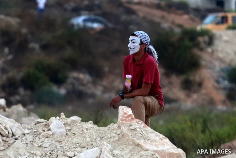 A masked Palestinian protester looks on during clashes with Israeli soldiers close to the Jewish settlement of Bet El, in the West Bank city of Ramallah on October 4, 2015 after Israel barred Palestinians from Jerusalem'...