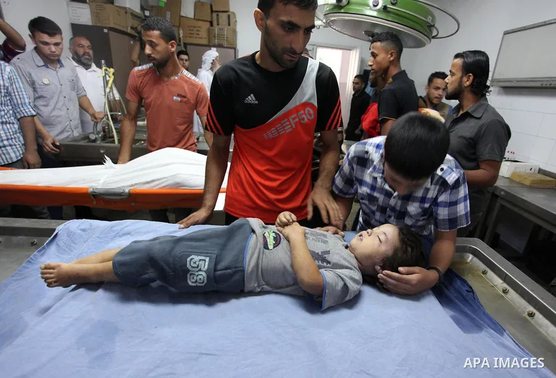 People stand around the body of a three-year-old Palestinian girl who was killed after her house was brought down by an Israeli air strike in Gaza early on October 11, 2015. An Israeli air strike on a Hamas target in the...