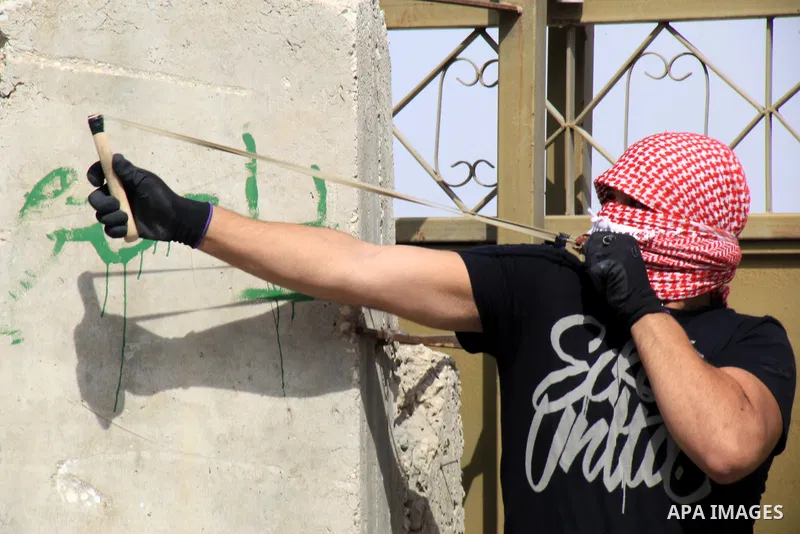 A Palestinian protester uses a sling shot to throw stones at Israeli police during clashes in Jabal al-Mukaber neighborhood, southern Jerusalem, on October 13, 2015. A wave of stabbings that hit Israel, Jerusalem and the...