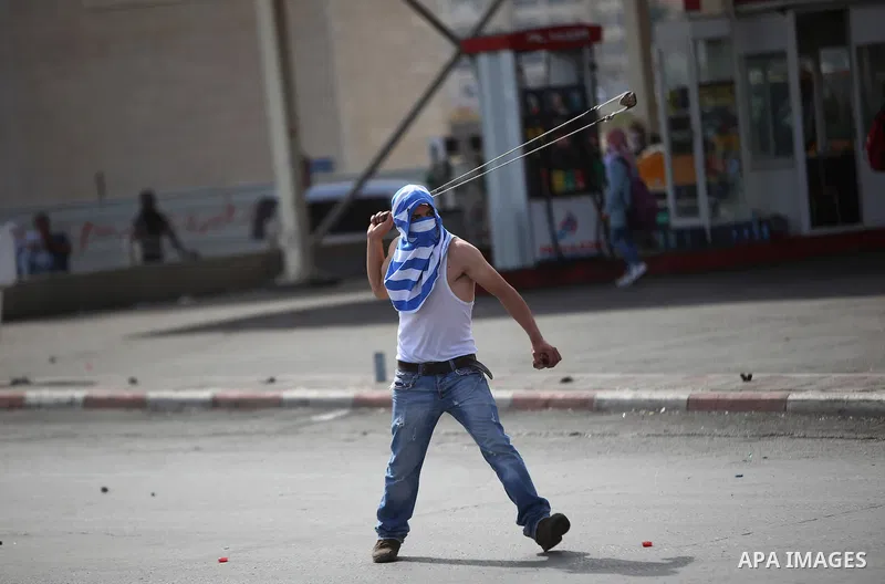 A Palestinian protester uses a sling shot to throw stones at Israeli security forces during clashes near the Jewish settlement of Bet El, near the West Bank city of Ramallah, on October 13, 2015. A wave of stabbings that...