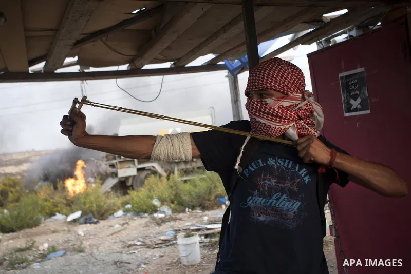 A Palestinian protester uses a sling shot to throw stones at Israeli security forces during clashes near the Jewish settlement of Bet El, near the West Bank city of Ramallah, on October 13, 2015. A wave of stabbings that...