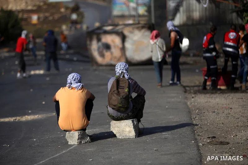 Palestinian protesters sit on the road during clashes with Israeli security forces near the Jewish settlement of Bet El, near the West Bank city of Ramallah, on October 14, 2015. Seven Israelis and 30 Palestinians, inclu...