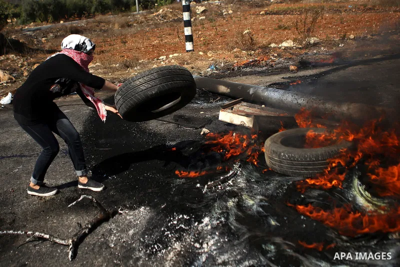 A female Palestinian protester burns tires during clashes with Israeli security forces near the Beit El settlement on the outskirts of Ramallah in the West Bank, on October 16, 2015. The unrest that has engulfed Jerusale...