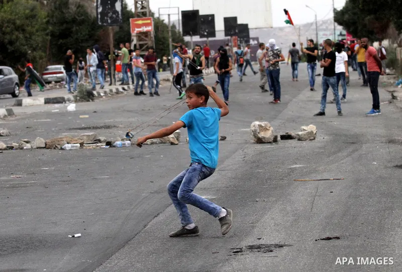 A Palestinian youth uses a sling shot to throw stones during clashes with Israeli security forces at the Hawara checkpoint, south of the West Bank city of Nablus on October 22, 2015. Palestinian factions called for mass...