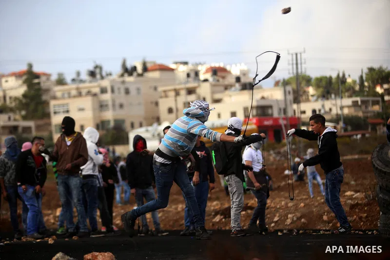 Masked Palestinian protesters use sling shots to throw stones towards Israeli security forces during clashes near the Jewish settlement of Beit El, near the West Bank city of Ramallah October 27, 2015. The current round...