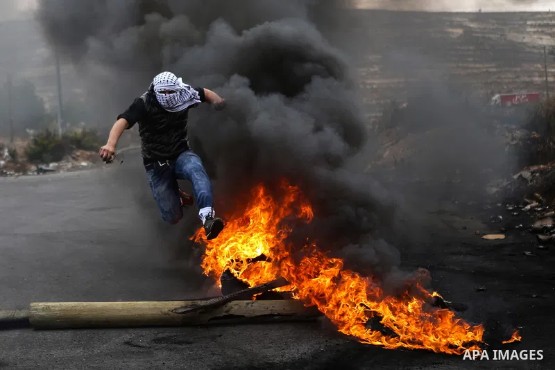 A masked Palestinian protester jumps over burning tires during clashes with Israeli security forces near the Jewish settlement of Beit El, near the West Bank city of Ramallah October 27, 2015. The current round of violen...