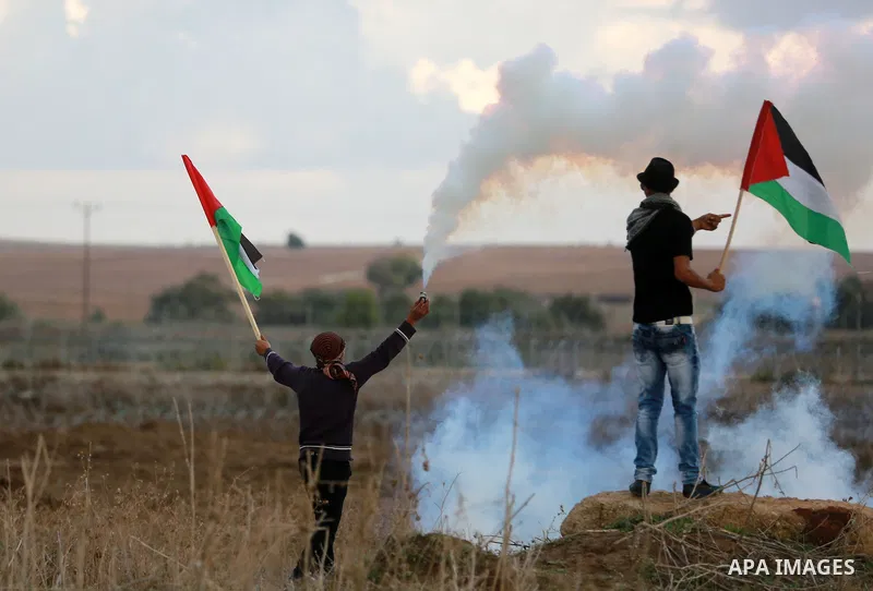 A Palestinian protester waving his national flag as he holds a tear gas canister fired by Israeli troops during clashes near the border between Israel and Central Gaza Strip October 27, 2015. The current round of violenc...