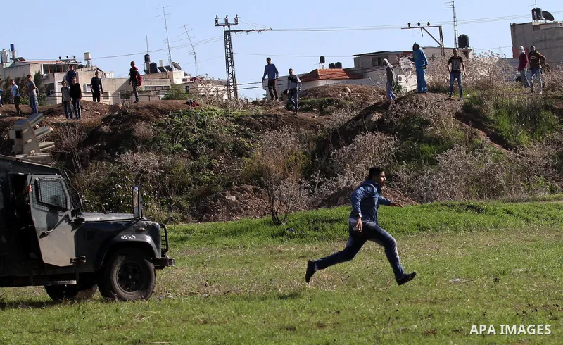 A Palestinian protester runs in front of an Israeli military vehicle during clashes in the West Bank city of Tulkarm November 12, 2015. Israeli undercover forces raided a hospital in the West Bank on Thursday, shooting d...