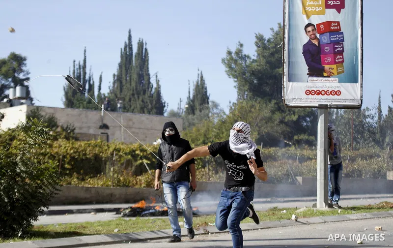 A Palestinian protester uses a sling shot to throw stones towards israeli security forces during clashes on the main road in West Bank town of Halhul that connects the village with Hebron city on November 14, 2015, after...