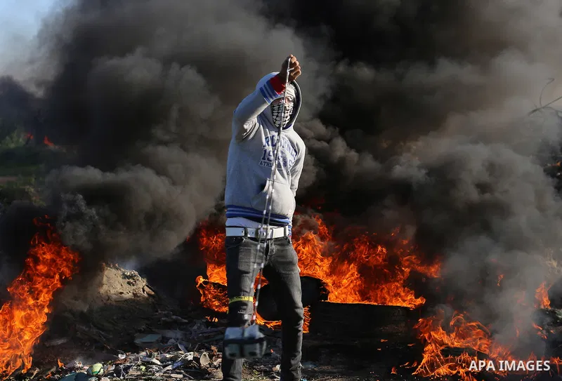 A Palestinian protester, standing in front of burning tires, uses a slingshot to hurl stones towards Israeli security forces during clashes along the border with Israel in the eastern suburbs of Gaza City on December 4,...