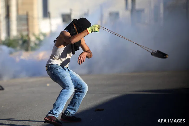 A Palestinian protester uses a slingshot to hurl stones towards Israeli security forces during clashes following killed of Abed al-Rahman al-Barghouthi, 27 in the West bank village of Aboud near Ramallah on December 04,...