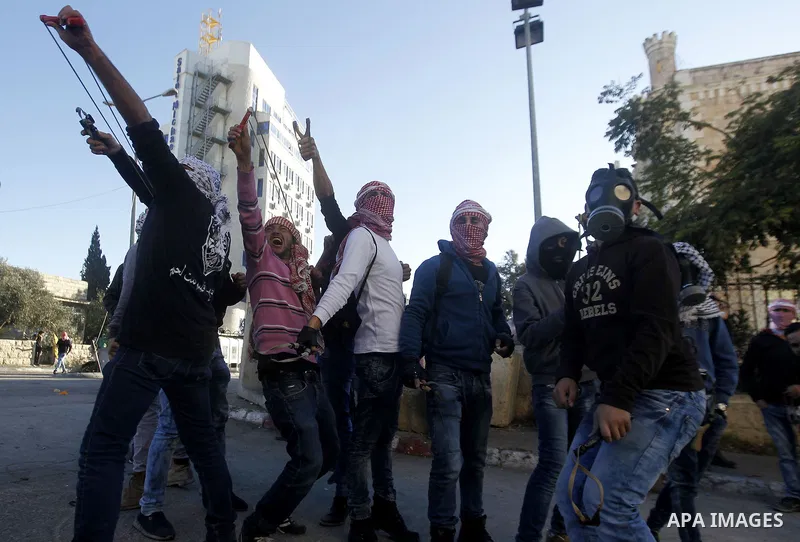 Palestinian protestesr use a slingshot to throw stones towards Israeli security forces during clashes at the main entrance of the West Bank city of Bethlehem on December 8, 2015 after the funeral of Palestinian Malek Sha...