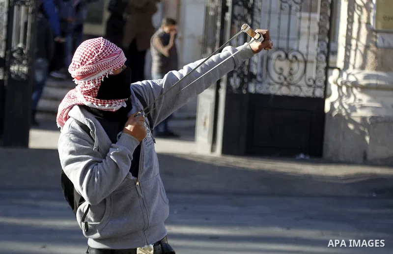 A Palestinian protester uses a slingshot to throw stones towards Israeli security forces during clashes at the main entrance of the West Bank city of Bethlehem on December 8, 2015 after the funeral of Palestinian Malek S...
