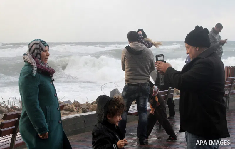 Palestinians stand in front of beach of Gaza city as waves crash fishermen's harbor during a rainy day on the first day of the new year on Jan. 01, 2016. Photo by Mohammed Asad