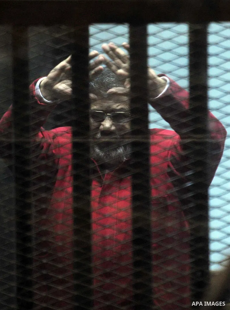 Ousted Egyptian president Mohammed Morsi gestures as he sits behind bars during his trail as part of the so-called 'Qatar espionage' case, in a court in Cairo on january 2, 2015. The defendants are accused of 'leaking im...