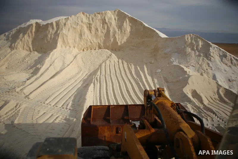 A Palestinian worker uses a bulldozer to load the salt extraction "raw material" from the Dead Sea, in the West Bank city of Jericho on January 14, 2016. The Dead Sea also called the Salt Sea, is a salt lake with borders...