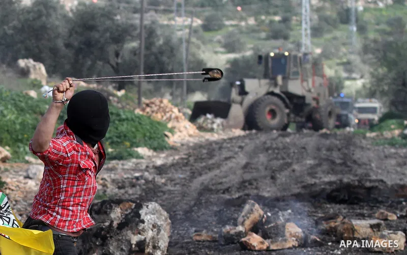 A Palestinian protester uses a slingshot to hurl stones toward Israeli security forces during clashes following a protest against the expropriation of Palestinian land by Israel in the West Bank village of Kafr Qaddum, n...
