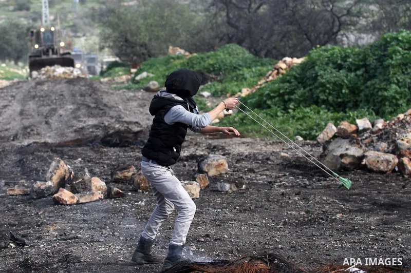 A Palestinian protester uses a slingshot to hurl stones toward Israeli security forces during clashes following a protest against the expropriation of Palestinian land by Israel in the West Bank village of Kafr Qaddum, n...
