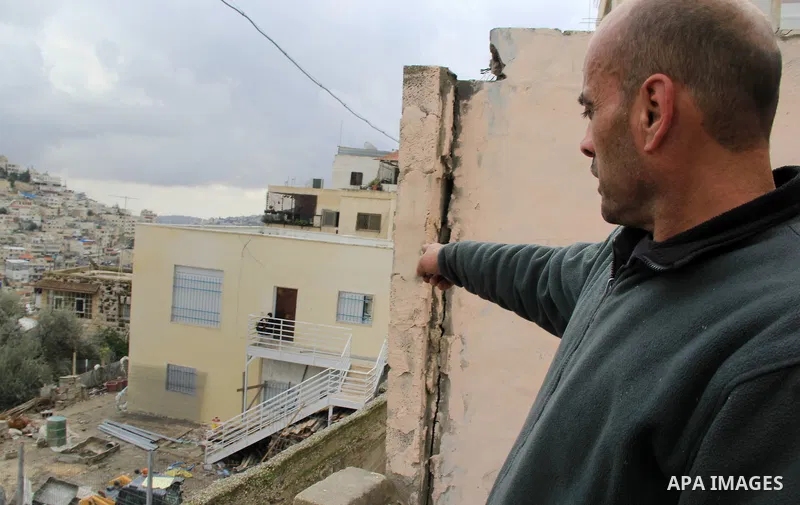 A Palestinian man looks on Israeli settlers as they sit on the balcony of house which the Palestinian Abu Tir family has for years that was taken over by Israeli settlers backed by police in the East Jerusalem neighbourh...