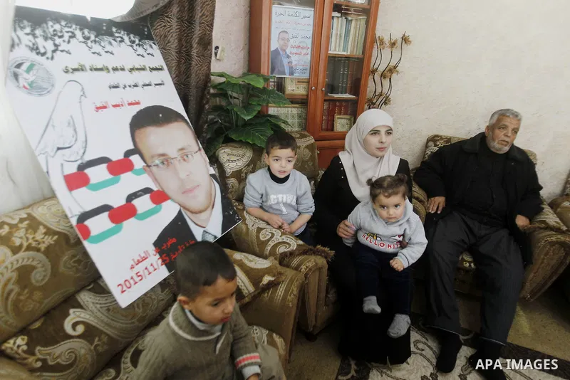 Fayha Shalash, the wife of Palestinian journalist Mohammed al-Qiq (portrait) who is on hunger strike, sits with her family at her home in the West Bank village of Dura on January 20, 2016. Qiq, a 33-year-old reporter for...