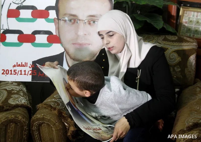 Fayha Shalash, the wife of Palestinian journalist Mohammed al-Qiq (portrait) who is on hunger strike, sits with her son at her home in the West Bank village of Dura on January 20, 2016. Qiq, a 33-year-old reporter for Sa...