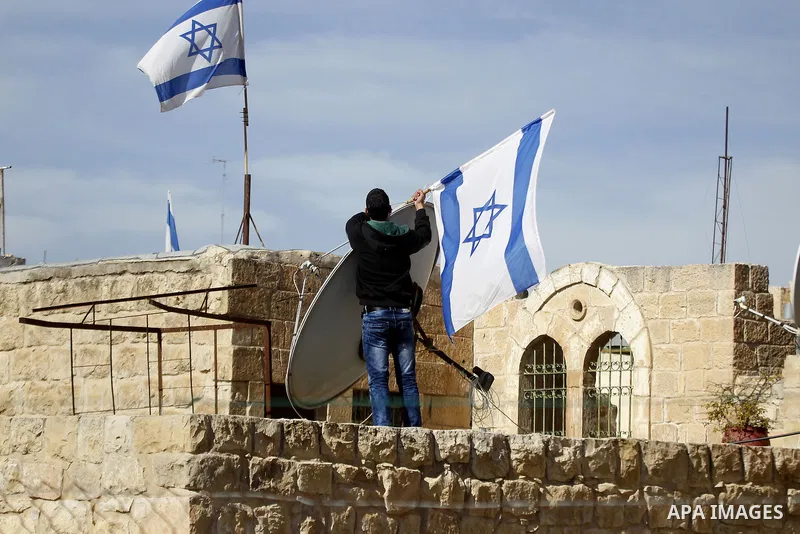 A Palestinian man removes the Israeli flag from a house as dozens of settlers were evacuated by Israeli security forces from two homes in the heart of the West Bank city of Hebron on January 22, 2016, the day after they...