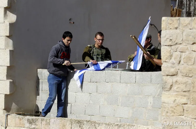 A Palestinian man removes the Israeli flag from a house as dozens of settlers were evacuated by Israeli security forces from two homes in the heart of the West Bank city of Hebron on January 22, 2016, the day after they...