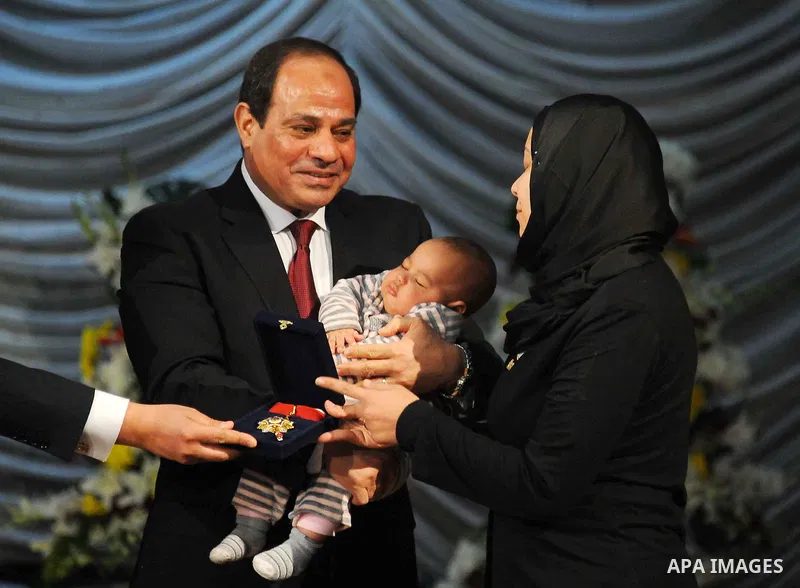 Egyptian President Abdel-Fattah el-Sissi holds a child as he presents a medal to the widow of a policeman killed in militant attacks, at a ceremony marking Police Day, which falls on Jan. 25, the anniversary of the 2011...