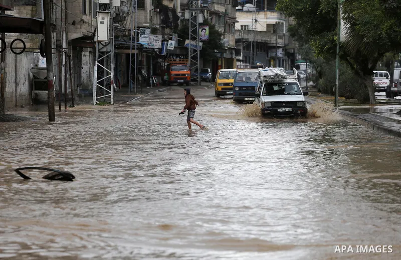 Palestinian boys walk though a flooded road on a rainy day in Gaza city, January 24, 2016. Photo by Mohammed Asad