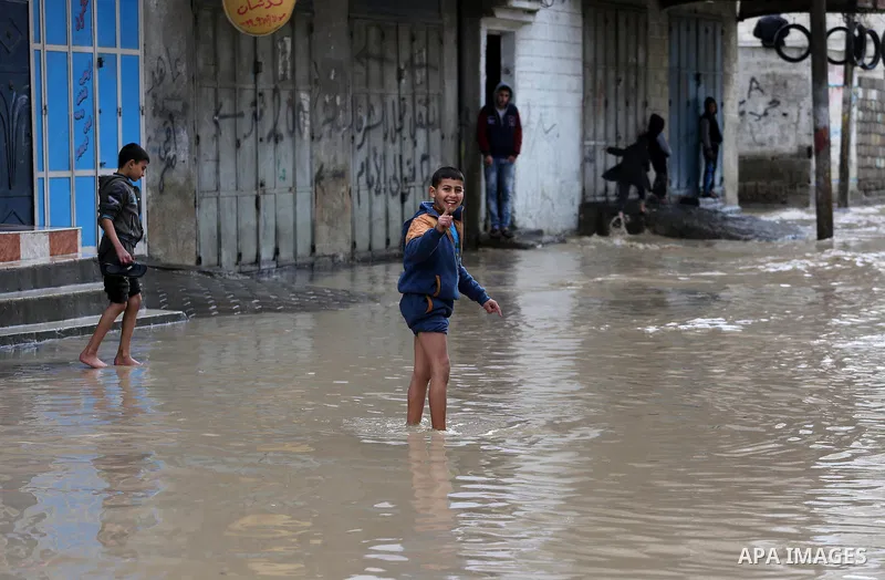 Palestinian boys walk though a flooded road on a rainy day in Gaza city, January 24, 2016. Photo by Mohammed Asad