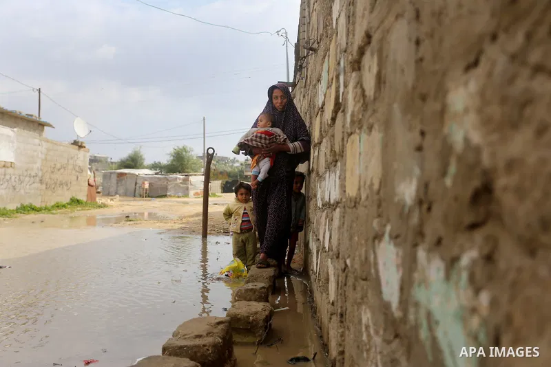 A Palestinian woman holds her son as she crosses a road flooded with rainwater following heavy rains, in Khan Younis in the southern Gaza Strip January 24, 2016. Photo by Yasser Qudih
