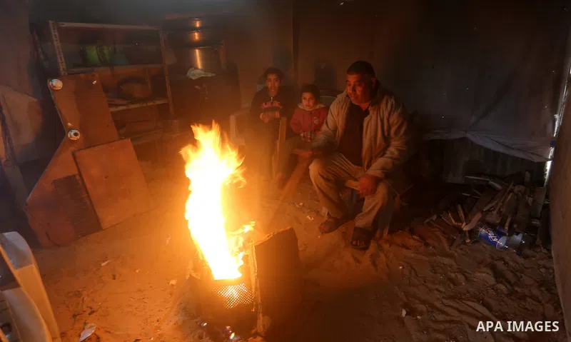 Members of a Palestinian famil warm themselves next to a fire during a rainy day, in Khan Younis in the southern Gaza Strip, January 24, 2016. Photo by Yasser Qudih