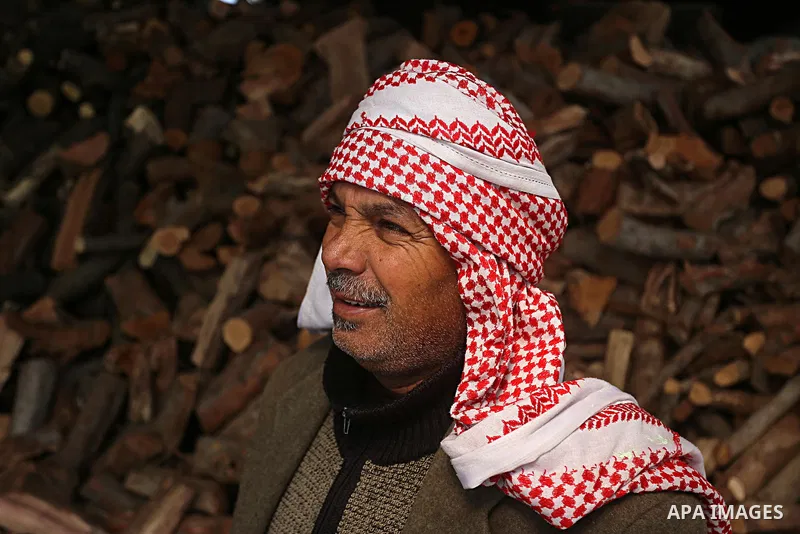 A Palestinian vendor stands in front of logs for heating and cooking on a rainy day, in Khan Younis in the southern Gaza Strip, January 24, 2016. Photo by Yasser Qudih