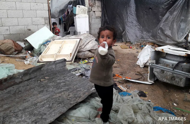 A Palestinian boy holds his milk bottle outside his family's dwelling on a rainy day, in Khan Younis in the southern Gaza Strip, January 24, 2016. Photo by Abed Rahim Khatib