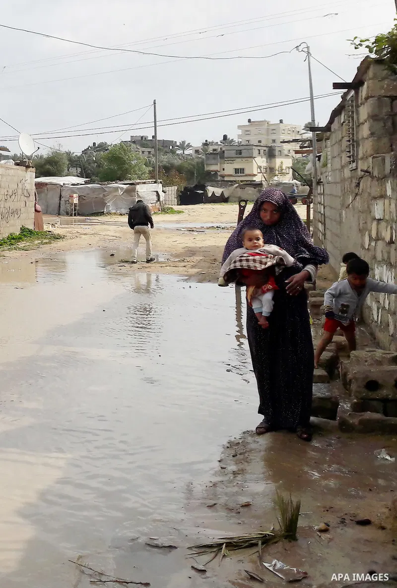 A Palestinian woman holds her son as she crosses a road flooded with rainwater following heavy rains, in Khan Younis in the southern Gaza Strip January 24, 2016. Photo by Abed Rahim Khatib