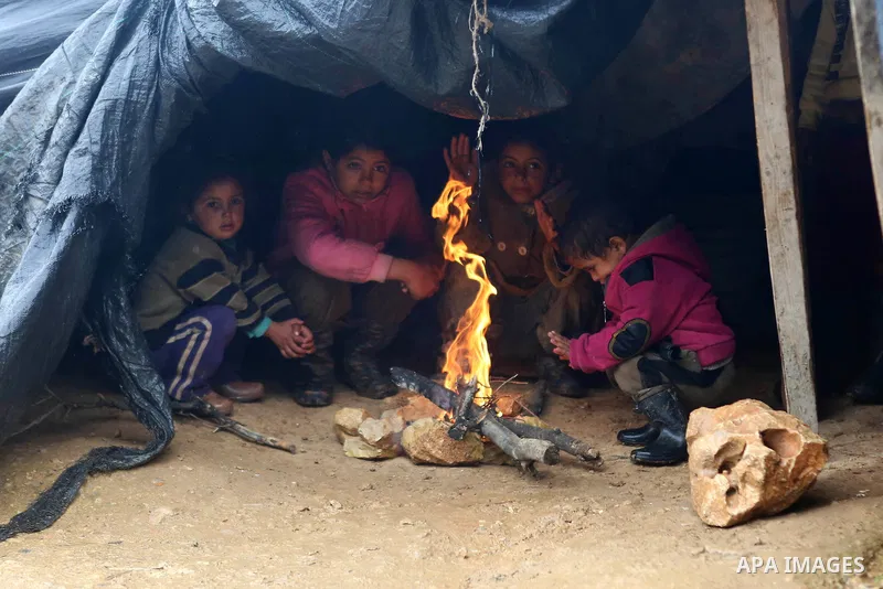Palestinian Bedouin children warm themselves next to a fire in their family's tent on a rainy day in the village of Ein Qiniya near the West Bank city of Ramallah, Jan. 25, 2016. Photo by Shadi Hatem