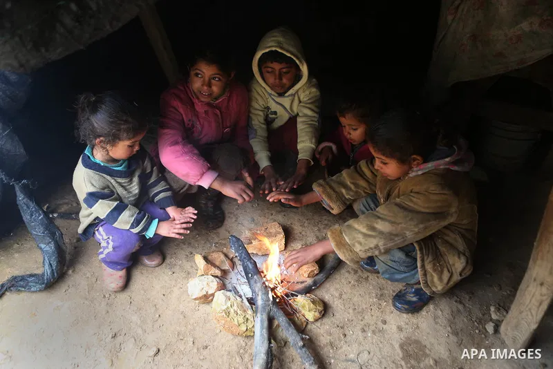 Palestinian Bedouin children warm themselves next to a fire in their family's tent on a rainy day in the village of Ein Qiniya near the West Bank city of Ramallah, Jan. 25, 2016. Photo by Shadi Hatem