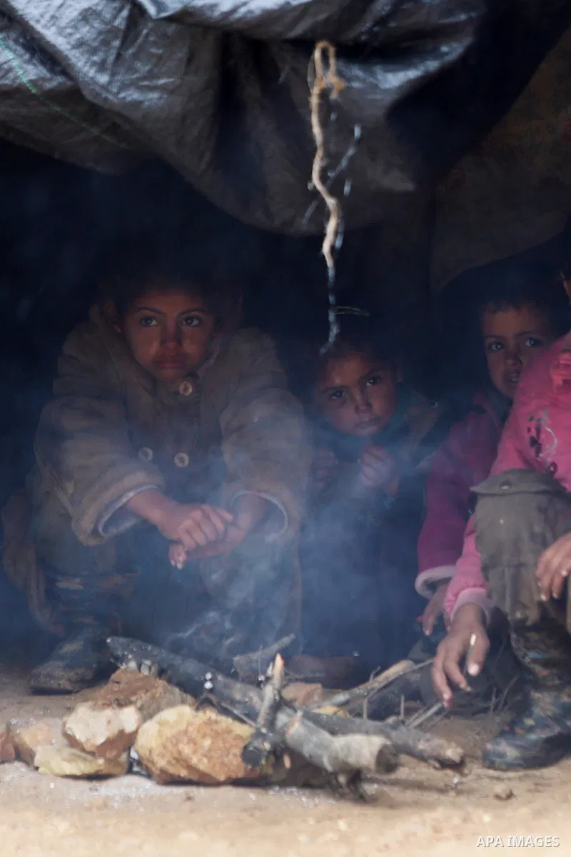 Palestinian Bedouin children warm themselves next to a fire in their family's tent on a rainy day in the village of Ein Qiniya near the West Bank city of Ramallah, Jan. 25, 2016. Photo by Shadi Hatem