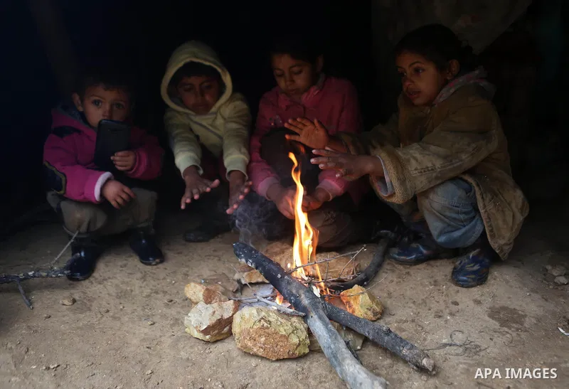 Palestinian Bedouin children warm themselves next to a fire in their family's tent on a rainy day in the village of Ein Qiniya near the West Bank city of Ramallah, Jan. 25, 2016. Photo by Shadi Hatem