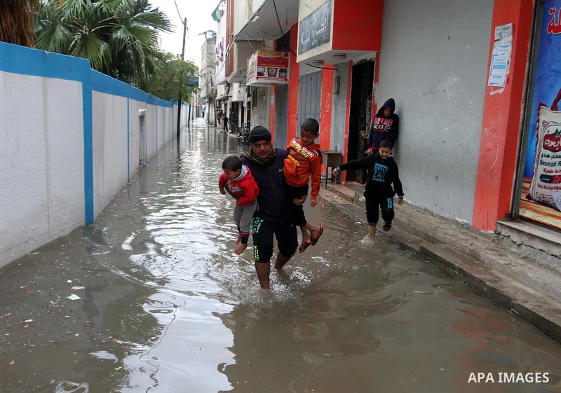 A Palestinian man holds his sons as he crosses a road flooded with rainwater following heavy rains, in Rafah in the southern Gaza Strip January 25, 2016. Photo by Abed Rahim Khatib
