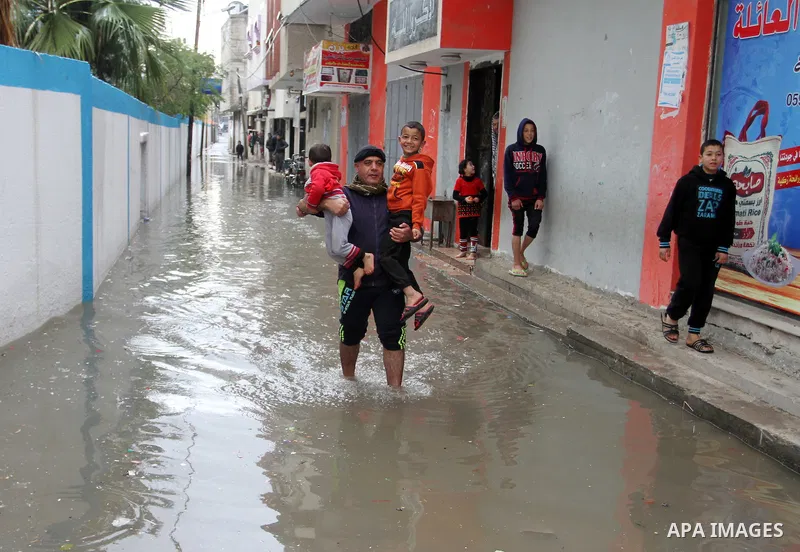 A Palestinian man holds his sons as he crosses a road flooded with rainwater following heavy rains, in Rafah in the southern Gaza Strip January 25, 2016. Photo by Abed Rahim Khatib