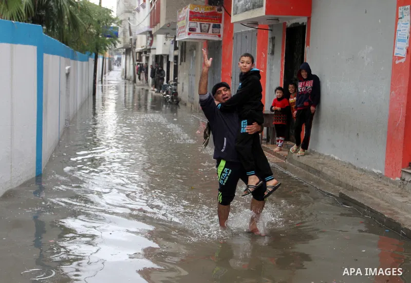A Palestinian man holds his sons as he crosses a road flooded with rainwater following heavy rains, in Rafah in the southern Gaza Strip January 25, 2016. Photo by Abed Rahim Khatib