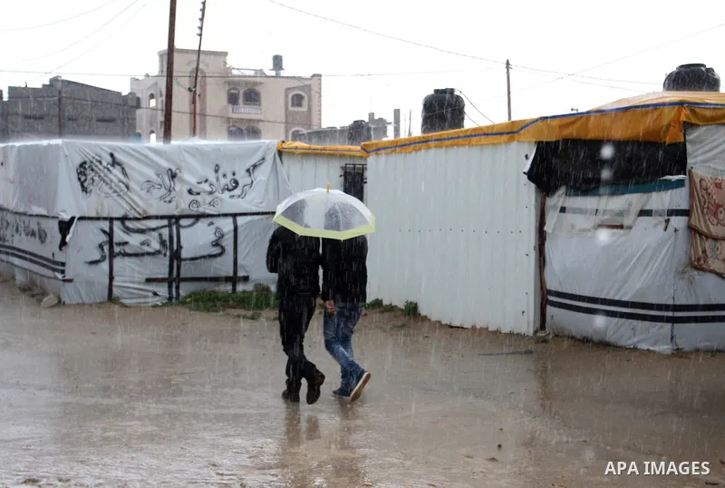 Palestinians walk past temporary housing during a winter storm in the southern Gaza Strip town of Khan Younis on January 25, 2016. Photo by Abed Rahim Khatib