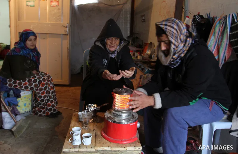 A Palestinian family sits around a heater in their temporary housing during a winter storm in the southern Gaza Strip town of Khan Younis on January 25, 2016. Photo by Abed Rahim Khatib
