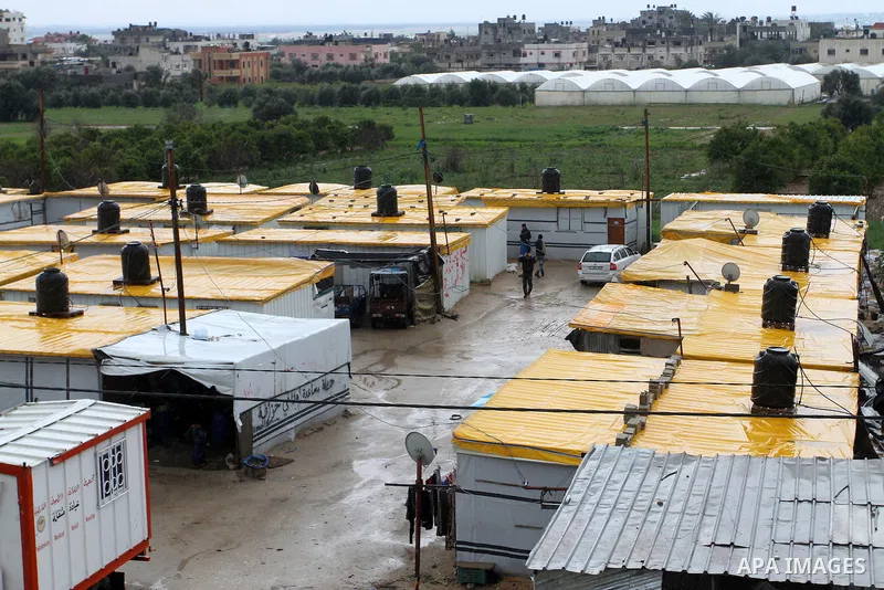 Palestinians walk past temporary housing during a winter storm in the southern Gaza Strip town of Khan Younis on January 25, 2016. Photo by Abed Rahim Khatib