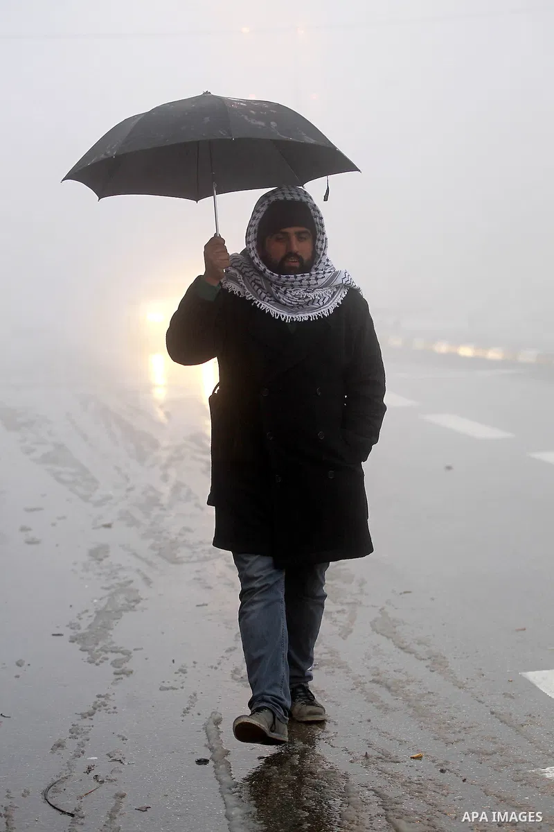 A Palestinian man holds umprella as he walks at a street during a snow storm in the West Bank village of Halhul, near Hebron, on Jan. 25, 2016. Photo by Wisam Hashlamoun