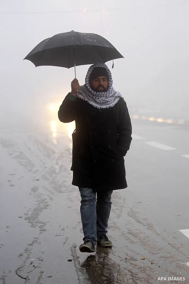 A Palestinian man holds umprella as he walks at a street during a snow storm in the West Bank village of Halhul, near Hebron, on Jan. 25, 2016. Photo by Wisam Hashlamoun