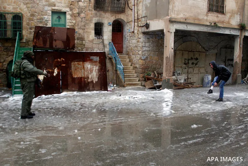 Israeli soldiers forces check Palestinians as they cross the street during a snowstorm in the West Bank city of Hebron, on January 26, 2016. Photo by Wisam Hashlamoun