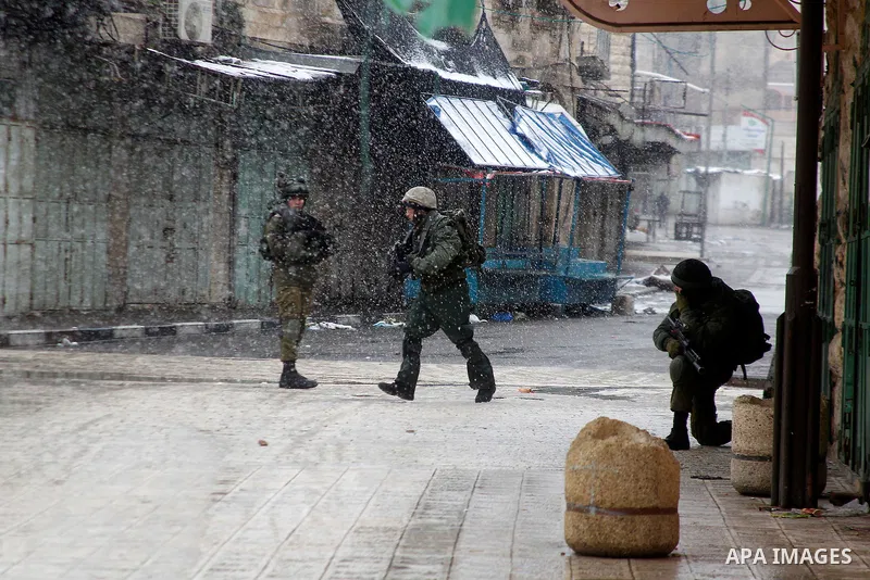 Israeli soldiers forces stand guard despite of the snow during a snowstorm in the West Bank city of Hebron, on January 26, 2016. Photo by Wisam Hashlamoun